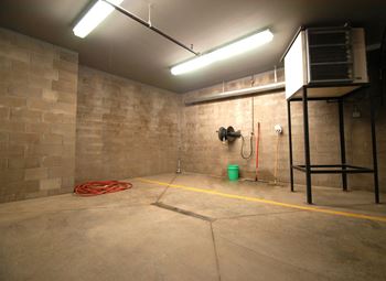Garage wash station in concrete underground parking garage, with several hoses and buckets for washing
